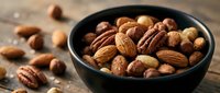 Mixed nuts and almonds in dark bowl on rustic wooden table for healthy snacking and cooking ingredients.