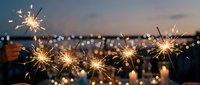 Glowing sparklers light up evening celebration with blurred crowd and bokeh lights in background, perfect for festive event marketing and holiday promotions.