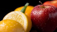 Fresh red apple and sliced orange with water drops on dark background, macro shot showing juicy fruit texture and natural freshness in vibrant colors.