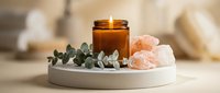 Spa wellness setup with burning candle, pink salt crystals and eucalyptus on tray for relaxation and aromatherapy treatments at home or salon.
