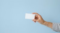 Caucasian hand holding blank white business card against light blue background for corporate branding and marketing purposes.