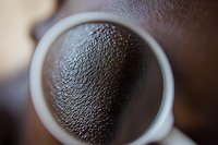 Close-up macro shot of dark roasted coffee grounds texture in white ceramic cup viewed from above, showing rich granular surface detail and fresh brewing preparation.
