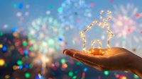 Hand holding glowing house symbol with warm lights against colorful bokeh background representing home protection, real estate dreams and property investment.