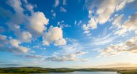 Dramatic sky with fluffy white clouds over rolling green hills and countryside landscape at sunset creating peaceful rural scenery for nature backgrounds.