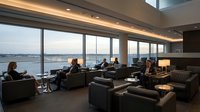 Business travelers relaxing in modern airport lounge with panoramic windows overlooking runway during evening hours for corporate travel and luxury service.