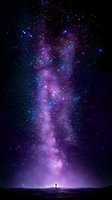 Silhouette of person standing beneath spectacular purple and blue night sky with bright Milky Way galaxy and countless stars creating magical cosmic atmosphere.