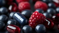 Fresh raspberry among dark blue and red supplement capsules and pills on black background, healthy lifestyle concept for wellness and nutrition.