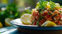 Fresh salmon tartare garnished with herbs and lemon wedges on white plate with blue rim, close up view of raw fish appetizer served in restaurant setting.