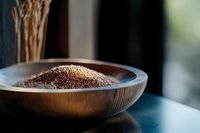 Raw red quinoa grains in wooden bowl on dark table with natural lighting, selective focus on nutritious ancient superfood grain for healthy cooking.