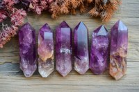 Purple amethyst crystal points arranged in row on rustic wooden surface with dried pink flowers, showcasing natural mineral formation and metaphysical healing properties.