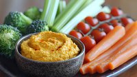 Fresh vegetable crudités platter with homemade pumpkin hummus dip in stone bowl, featuring carrots, celery, broccoli and cherry tomatoes for healthy snacking.