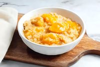 Creamy oatmeal porridge topped with fresh mandarin orange segments and honey drizzle in white ceramic bowl on wooden serving board against marble surface.