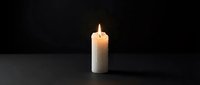 Single white candle with bright flame burning on dark surface against black background creating warm atmospheric lighting for meditation and relaxation.