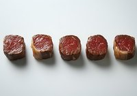 Five pieces of raw beef tenderloin steaks lined up showing different degrees of doneness from rare to well done on white background for culinary and cooking concepts.
