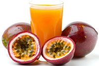 Passion fruit juice in glass with fresh whole and halved fruits on white background, ready for beverage, health, nutrition, and tropical drink design projects.