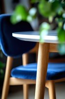 Modern round white table with wooden leg and navy blue velvet chair in background, selective focus creates soft blur effect for interior design and furniture styling.