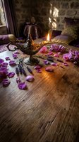 Ornate oil lamp with burning flame surrounded by purple rose petals and lavender sprigs on rustic wooden table in cozy stone cottage interior for aromatherapy relaxation.