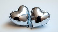 Metallic silver heart-shaped balloons on light background, romantic celebration decor for wedding, anniversary or Valentine's day party decoration.