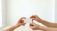 Close-up of two hands exchanging a blank white business card against a neutral background, suitable for corporate branding and professional networking concepts.