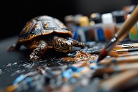 Box turtle walking through colorful oil paint palette with paintbrushes, artistic composition with selective focus and shallow depth of field.