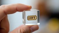 Hand holding transparent glass cube with golden gift label inside for business presentation and marketing concepts.
