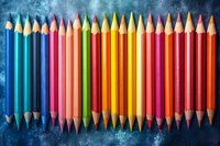 Vibrant colored pencils arranged in rainbow order on dark blue textured background. Creative art supplies composition for education and artistic projects.