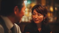 Asian businesswoman smiling during evening conversation with male colleague in upscale restaurant setting with warm ambient lighting for corporate dining concepts.