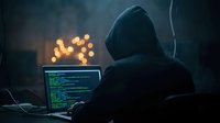 Anonymous hacker in dark hoodie working on laptop with code in dimly lit room with bokeh lights background for cybersecurity and technology concepts.