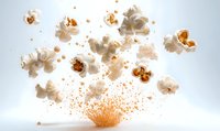 Popcorn kernels exploding in dynamic motion with flying white popped corn and orange butter splashes against light background, capturing moment of transformation.