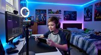 Young male gamer streaming in neon-lit bedroom setup with gaming headset, controller, and LED lighting for content creation and esports entertainment.
