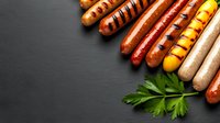 Grilled assorted sausages with grill marks arranged diagonally on dark slate background with fresh parsley leaf, copy space for menu design.