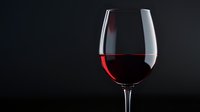 Red wine in elegant glass against dark background with dramatic side lighting creates moody atmosphere for restaurant, beverage, or culinary marketing.