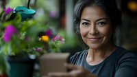 Middle-aged Asian woman smiling at camera surrounded by vibrant purple and yellow flowers in garden setting, wearing dark casual shirt, perfect for lifestyle and gardening content.