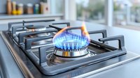 Blue flame burning on modern gas stove burner in kitchen, close up view showing energy consumption and cooking equipment. Professional culinary background.