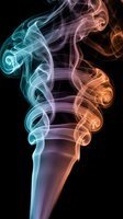Colorful smoke swirls in teal and orange tones rising against a dark black background, creating an abstract art effect.