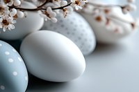 Pastel blue polka dot and white Easter eggs arranged with delicate cherry blossom branches creating soft spring holiday composition on light background.