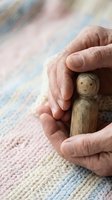 Elderly hands protectively cupping wooden figure symbolizing care, protection and support for vulnerable people in healthcare and social services.
