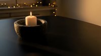 Lit white candle in rustic woven basket on dark wooden table with warm string lights creating cozy atmospheric home decor for relaxation and mindfulness.