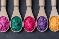 Vibrant colorful powder pigments in wooden spoons arranged in row on dark background, including pink, green, magenta, purple and yellow shades for natural cosmetics.