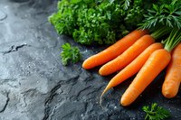 Fresh orange carrots with green leaves on dark stone background, raw organic vegetables for healthy eating and cooking. Food photography setup.