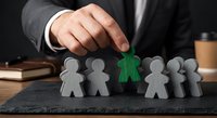 Professional businessman in suit selecting green paper figure from row of gray cutouts representing recruitment and talent acquisition in corporate environment.