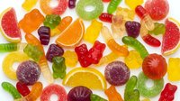 Colorful assorted gummy candies and fruit jellies scattered on white background. Sweet chewy treats in various shapes and flavors for confectionery designs.