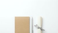 Minimalist kraft paper notebook with blank pages and white ribbon-tied scroll on clean white background for branding and stationery design projects.
