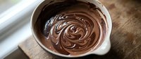 Melted chocolate swirled in white ceramic bowl on wooden surface, ready for baking, cooking, or dessert preparation projects.