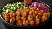 Spicy glazed shrimp bowl with fresh cucumber salad and pickled red onions, served on dark plate with dipping sauce, close up view of Asian fusion cuisine.