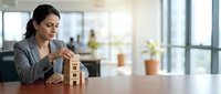 Professional Asian businesswoman building wooden block tower at modern office desk, strategic planning and goal achievement concept for corporate success.