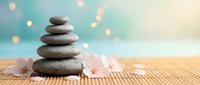 Zen stone stack with spa candles on bamboo mat creating peaceful meditation atmosphere with soft bokeh lights for wellness and relaxation concepts.