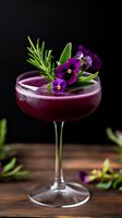 Purple cocktail in coupe glass garnished with fresh rosemary sprig, edible purple pansies, and cucumber on dark background. Elegant drink photography for bars and restaurants.