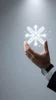Businessman hand holding glowing snowflake icon with sparkling effects against gray background for winter business concepts and holiday marketing campaigns.