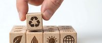 Hand placing wooden cube with recycling symbol on stack of eco-friendly blocks featuring sustainability icons for environmental awareness campaigns.
